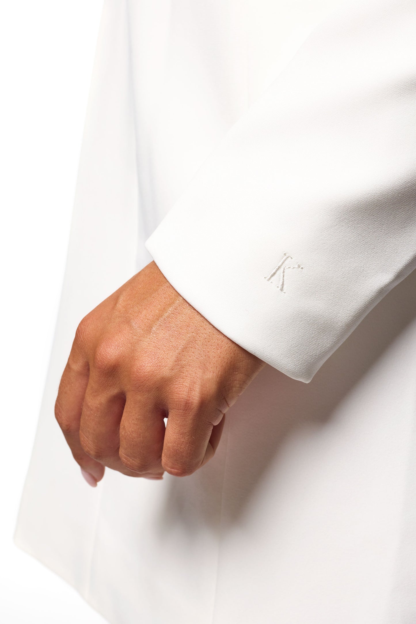 Close-up of The Kora Dress by KUOTES – luxury white tailored mini dress with subtle embossed ‘K’ detail on the sleeve, symbolising elegance and refinement."