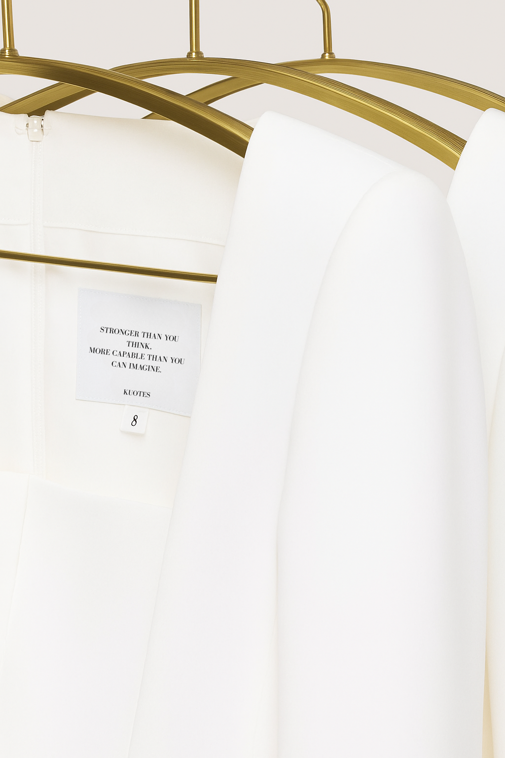 KUOTES Kora Dress in white hanging on a gold hanger, featuring inner label with empowering quote ‘Stronger than you think, more capable than you can imagine’ — minimalist luxury fashion designed to uplift, empower and inspire women.